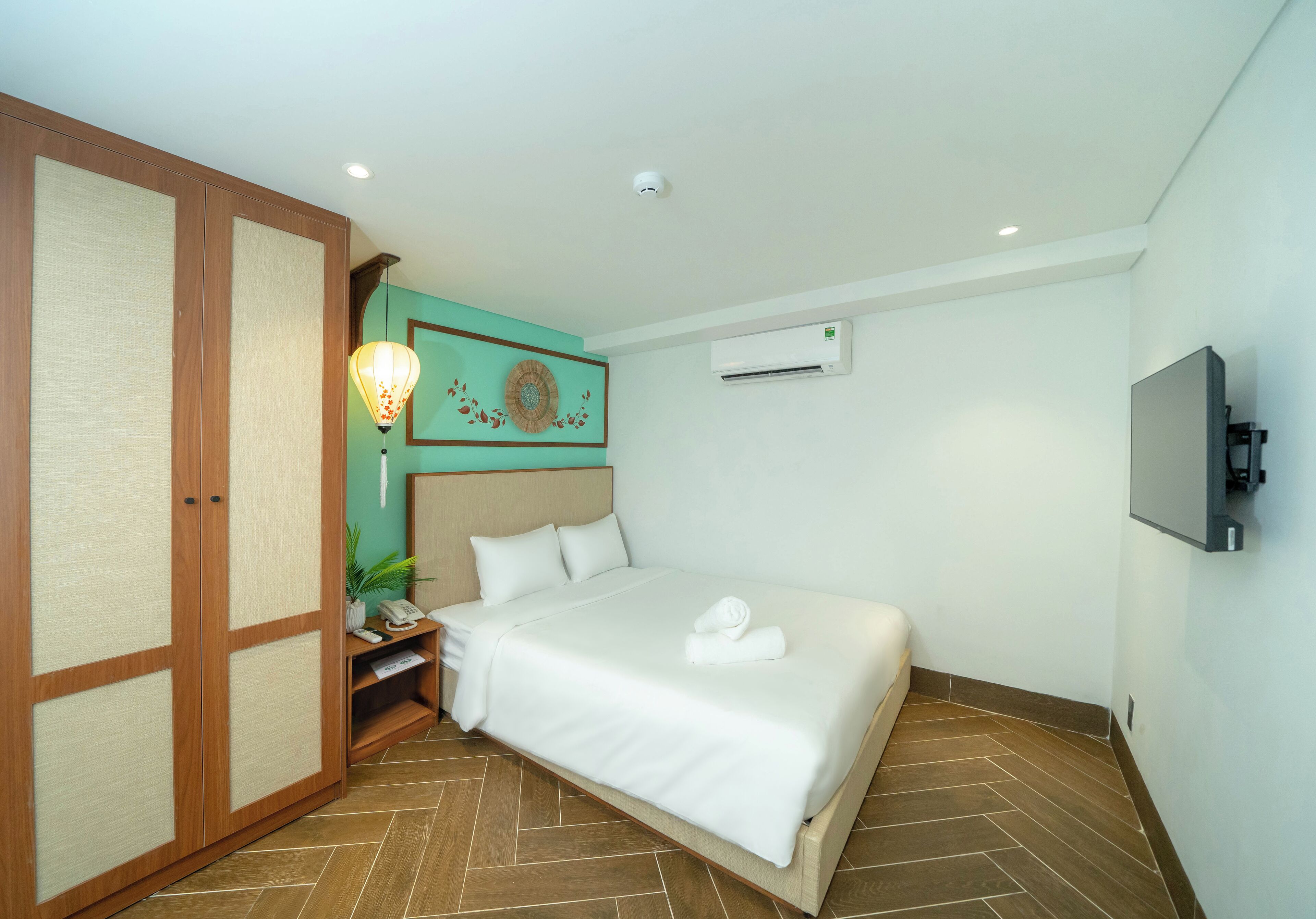 A hotel room with a bed, a TV, an air conditioning unit, and a wooden wardrobe.