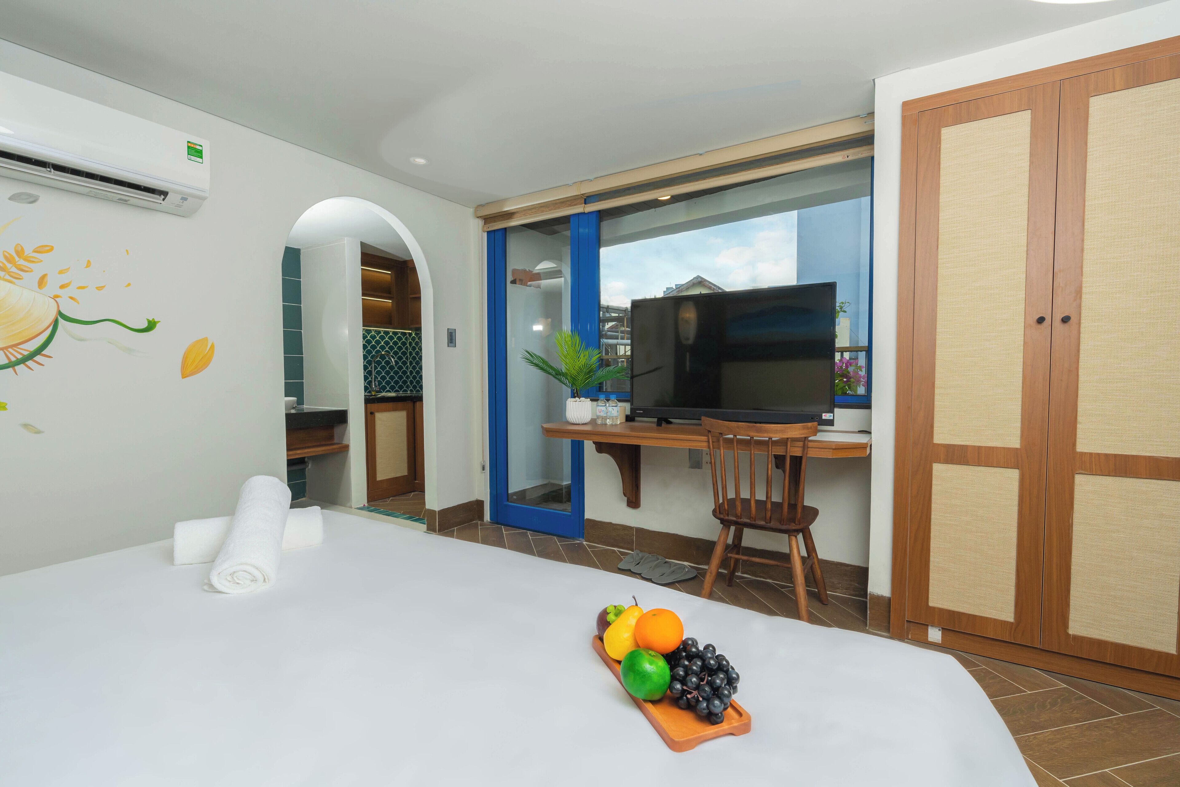 Een hotelkamer met een bed, een bureau met een televisie, een stoel en een schaal fruit.