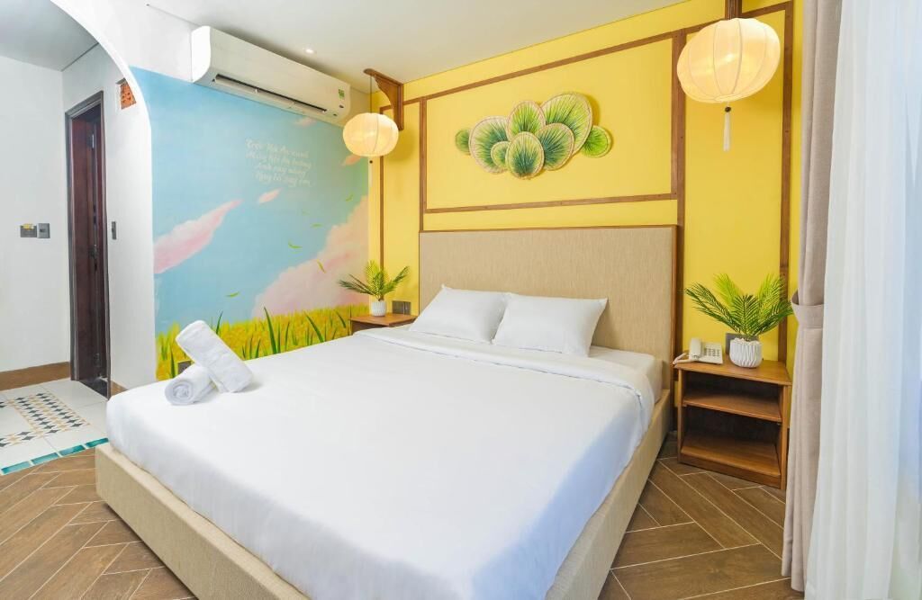 A hotel room with a large bed, a wall mural, a small table with a plant, and a nightstand with a lamp.