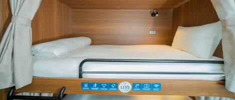 A compact, well-lit sleeping area with a single bed, a small table, and a curtain.