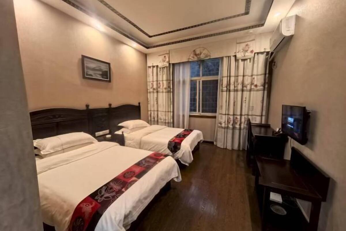 Une chambre d’hôtel avec trois lits, une télévision et une fenêtre avec des rideaux.