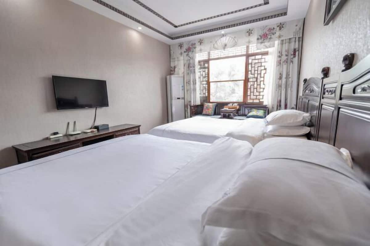 Une chambre d’hôtel avec deux lits, une télévision, un bureau avec un ordinateur et une fenêtre agrémentée de volets décoratifs.