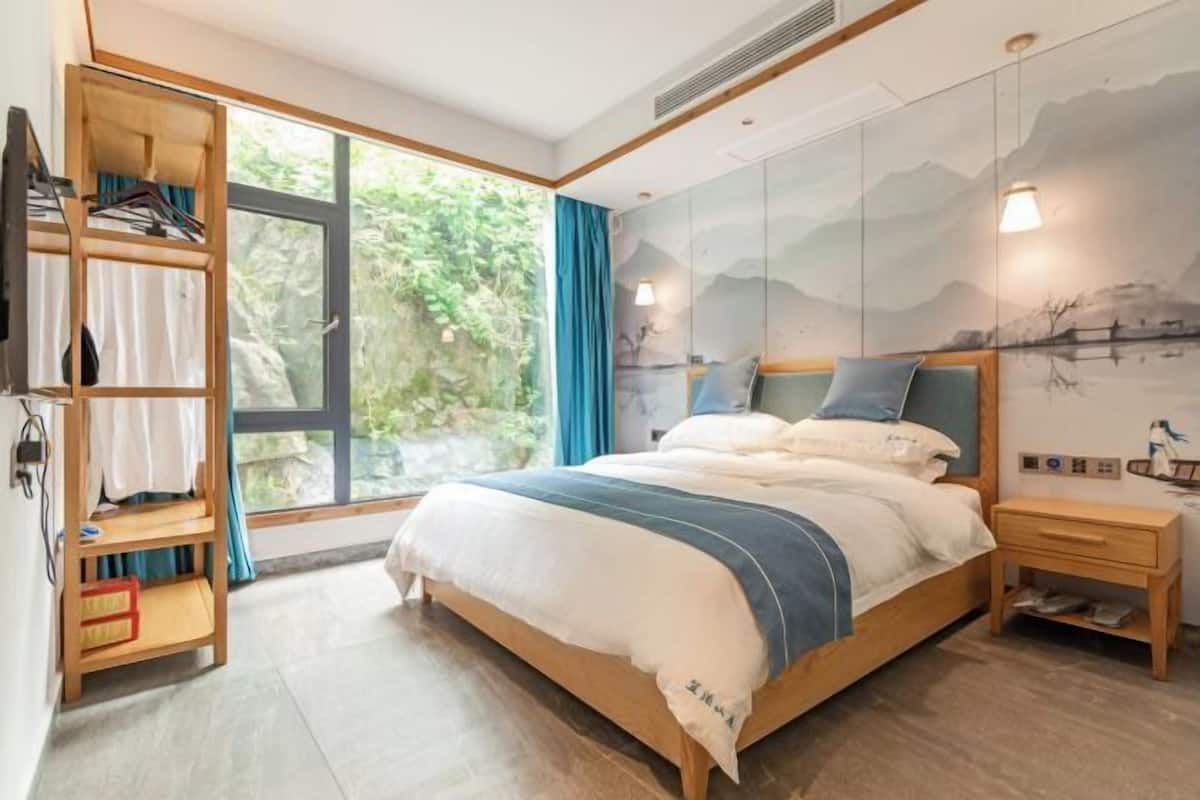 Une chambre à coucher comprenant un lit, une armoire, une table de chevet et une fenêtre donnant sur un paysage verdoyant.