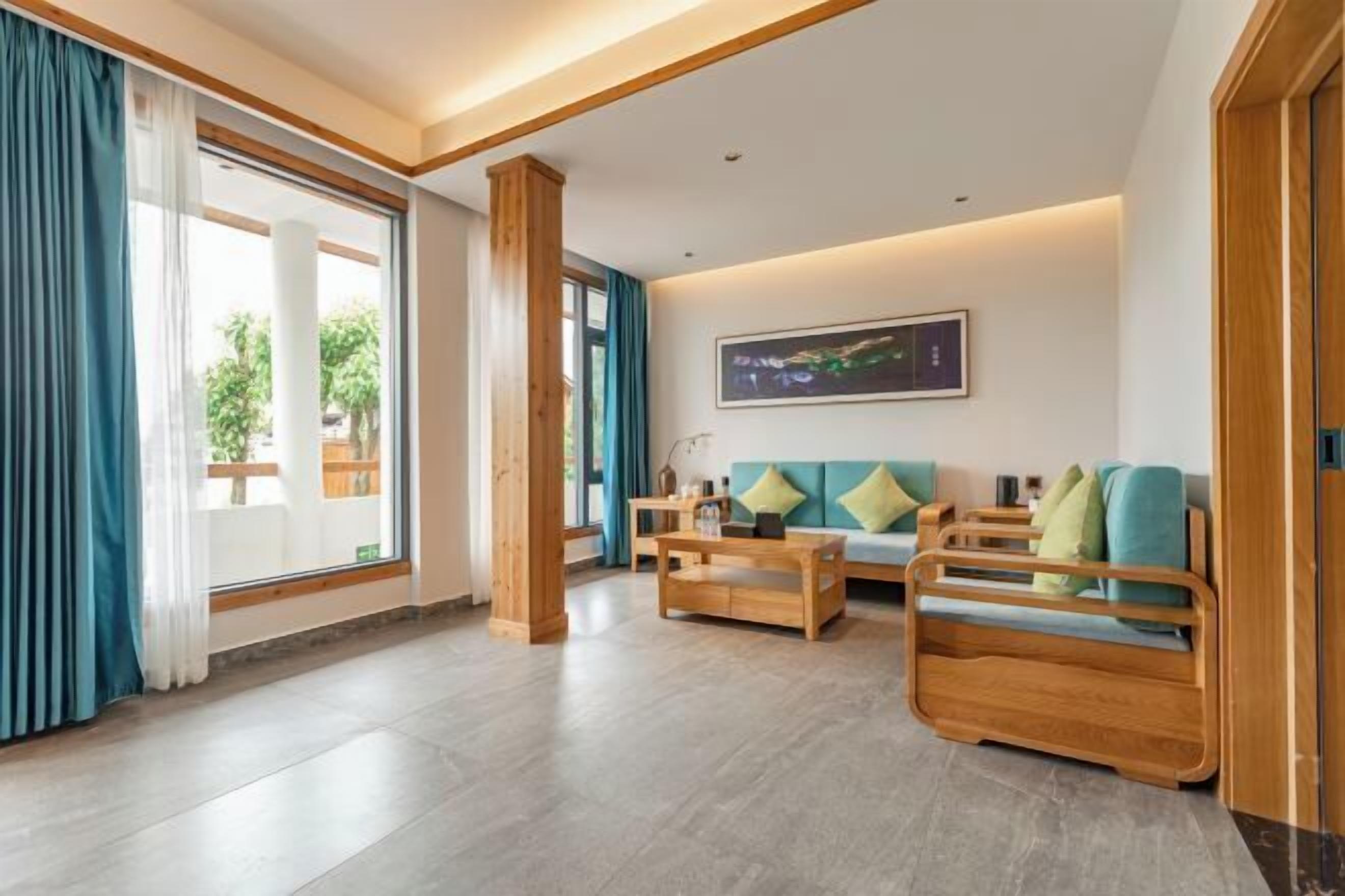 Amplia sala de estar con sofá, mesa de centro de madera y un ventanal con cortinas.