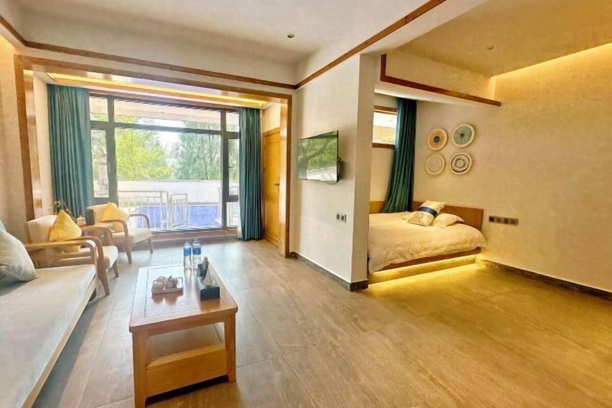 Une chambre d’hôtel comprenant un lit, un canapé, une table basse, une télévision et un balcon avec des rideaux.