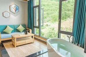 Ett rum med en soffa, ett soffbord i trä, ett badkar och stora fönster med gardiner.