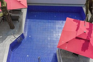 A blue tiled pool with a ladder, red umbrellas, and a tree. - Libo Boutique Guesthouse (Yongshun)
