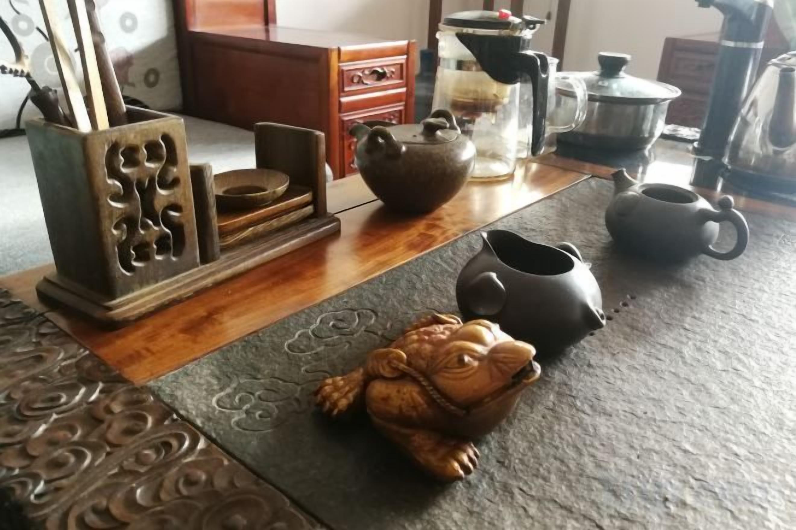 A traditional Japanese tea set on a tatami mat, a ceramic frog figurine, and a wooden cabinet with drawers.
