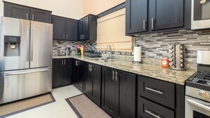 Uma cozinha moderna com armários escuros, eletrodomésticos de aço inoxidável, bancada de granito e painel de azulejos.