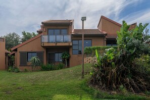 Une maison moderne à deux étages, dotée d’un balcon, d’un petit jardin et d’un lampadaire.