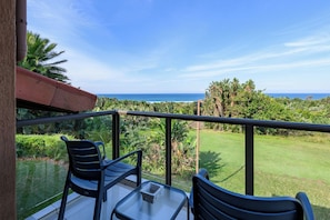 A balcony with two chairs and a table, overlooking a lush green landscape and the ocean. - San Lameer Villa 3706 (Southbroom)