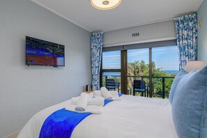A hotel room with a bed, a TV mounted on the wall, and a balcony with a view of the ocean. - San Lameer Villa 3706 (Southbroom)