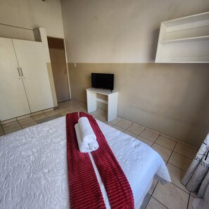 Une chambre d’hôtel avec un lit, un téléviseur posé sur une petite table et une armoire.