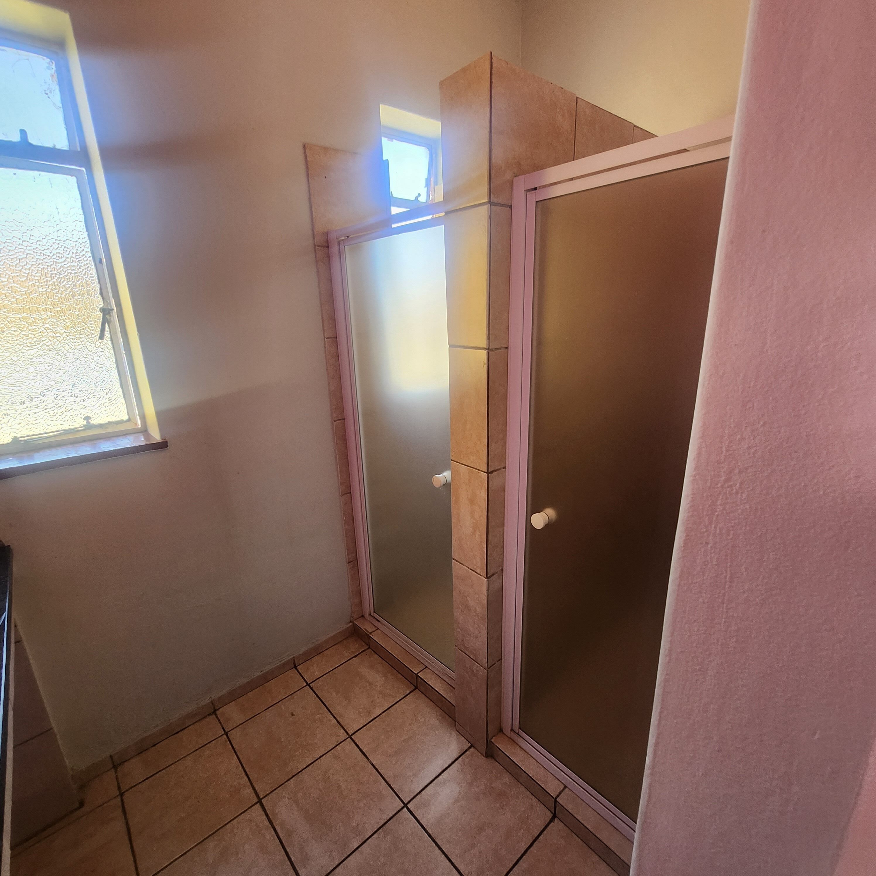 Een kleine badkamer met een douche, een raam en betegelde vloer.