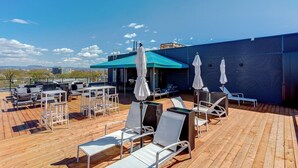 Een dakterras met zitplaatsen buiten, parasols en uitzicht op de skyline.