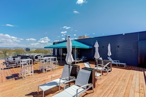 Eine Dachterrasse mit Sitzgelegenheiten im Freien, Sonnenschirmen und Blick auf die Skyline.