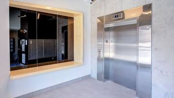 En moderne elevator med digitalt display, et vindue med træramme og en betonvæg.
