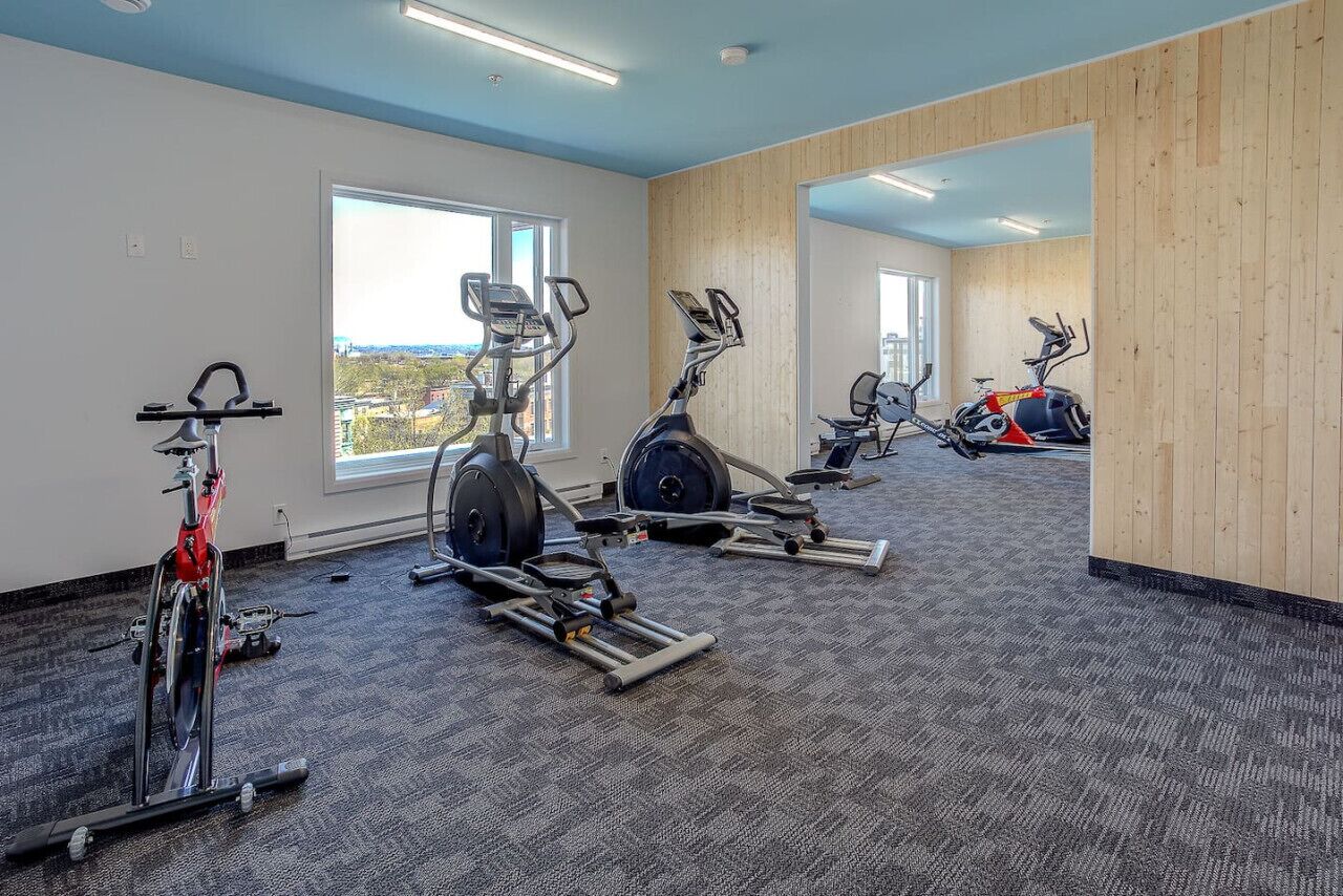 Et fitnesscenter med løbebånd, styrkeapparater og udsigt over byen.