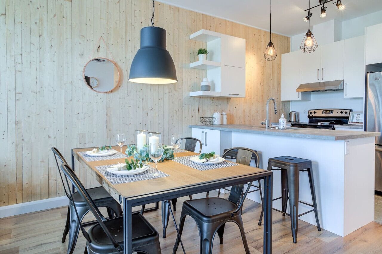 A modern kitchen with a central island, pendant lighting, and a dining area with a wooden table and chairs.