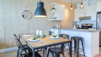 A modern kitchen with a central island, pendant lighting, and a dining area with a wooden table and chairs.
