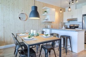 A modern kitchen with a central island, pendant lighting, and a dining area with a wooden table and chairs. - Sommet de la basse-ville / Downtown (Ville de Québec)