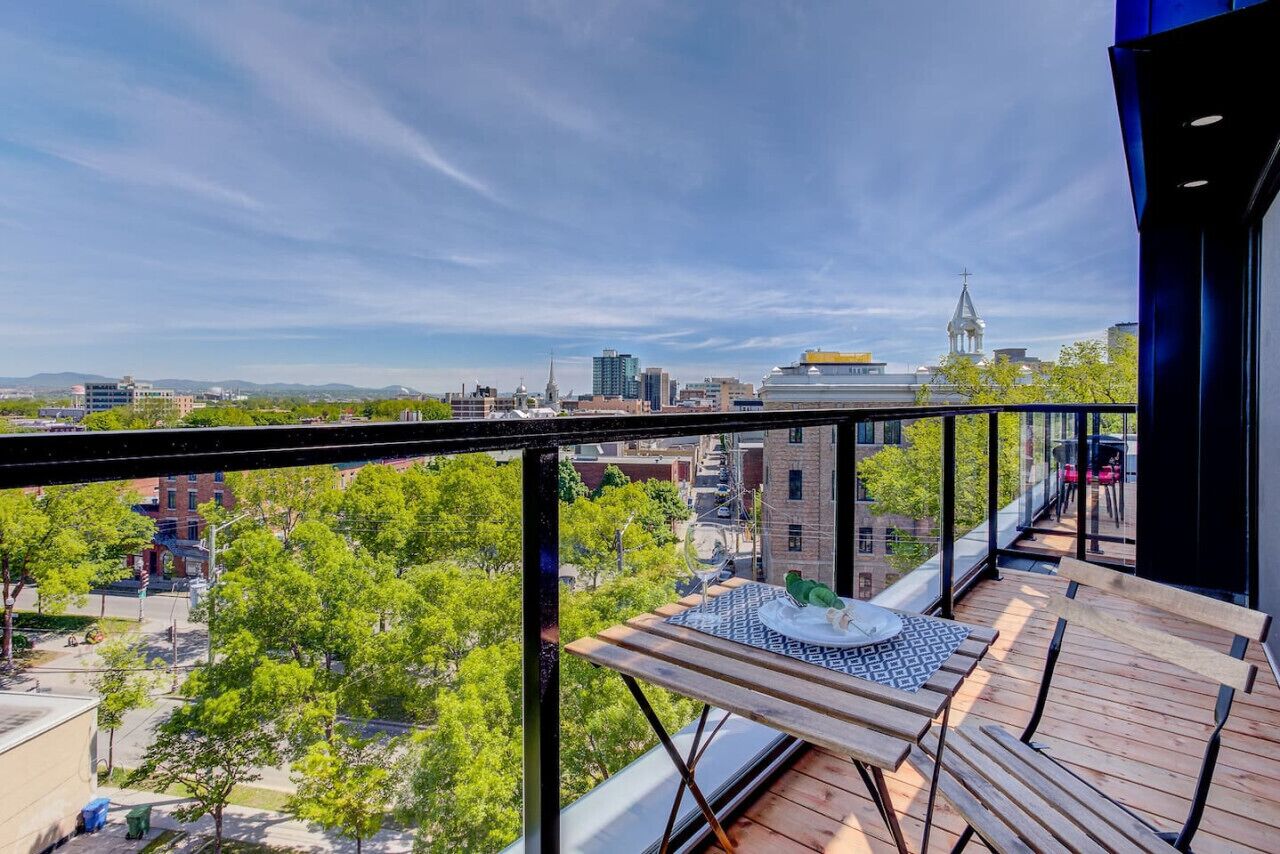 A balcony with a view of a cityscape, a table with a birdcage, and a bench.
