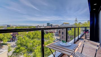 A balcony with a view of a cityscape, a table with a birdcage, and a bench.