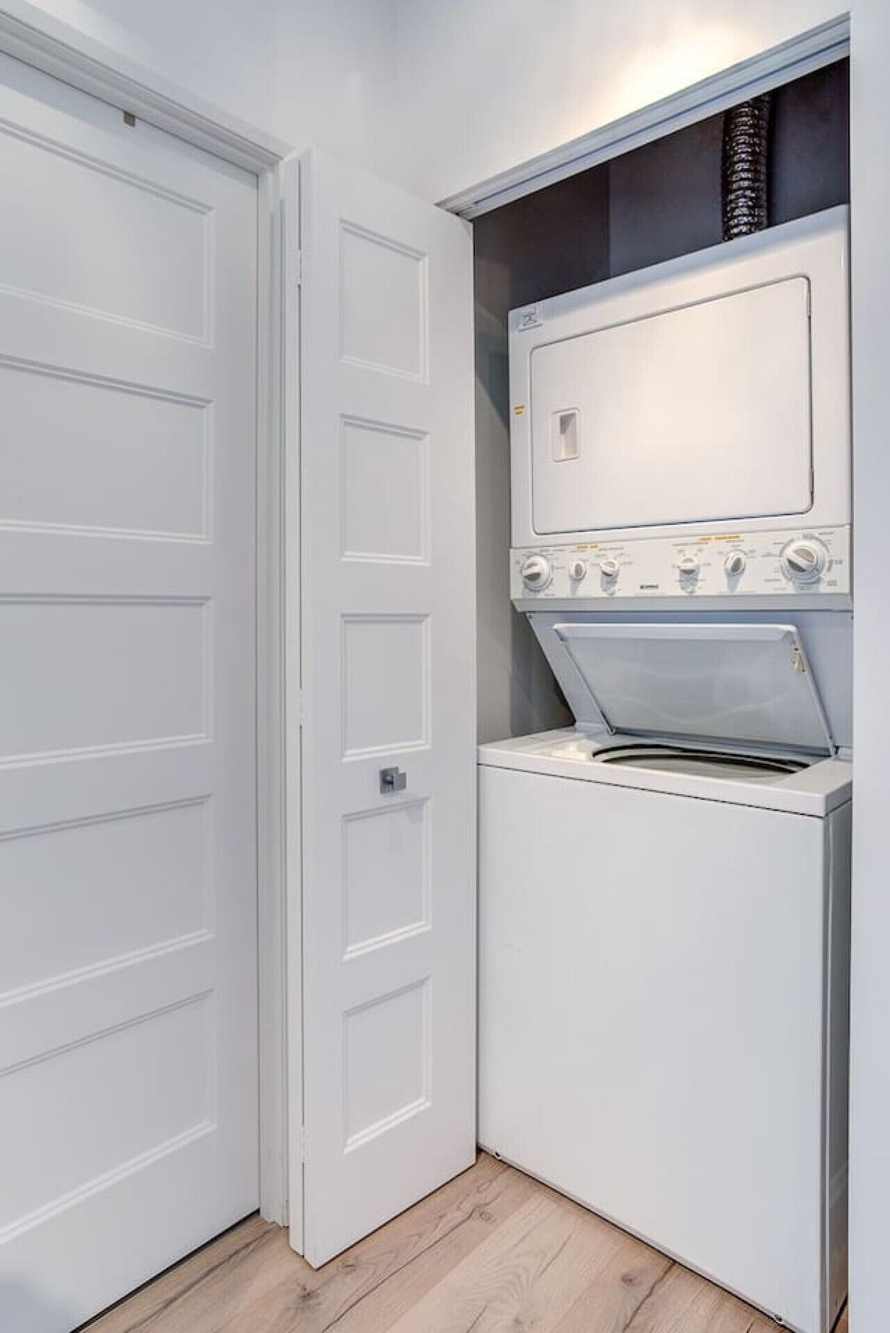 A compact laundry room with a washing machine and dryer, a white door, and a wooden floor.