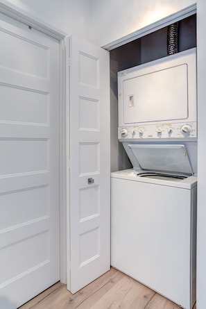 A compact laundry room with a washing machine and dryer, a white door, and a wooden floor. - Sommet de la basse-ville / Downtown (Ville de Québec)