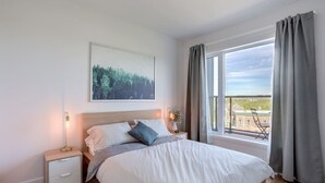 Een slaapkamer met een bed, nachtkastje, bedlampje en een raam met gordijnen.