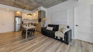 A modern kitchen with a dining area, a black sofa, and a white door. - Le Jules-Rooftop Pool (Québec)