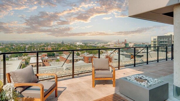 A rooftop terrace with two wooden chairs and a small planter, overlooking a cityscape with buildings and a distant smokestack. - Le Jules-Rooftop Pool (Québec)