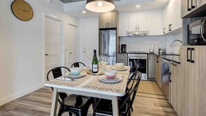 A modern kitchen with stainless steel appliances, a dining area with a table set for four, and light wood cabinetry. - Le Jules-Rooftop Pool (Québec)