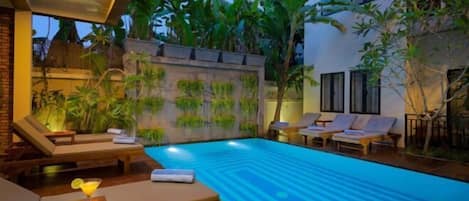 A swimming pool with lounge chairs and a bar area, surrounded by greenery and a stone wall.