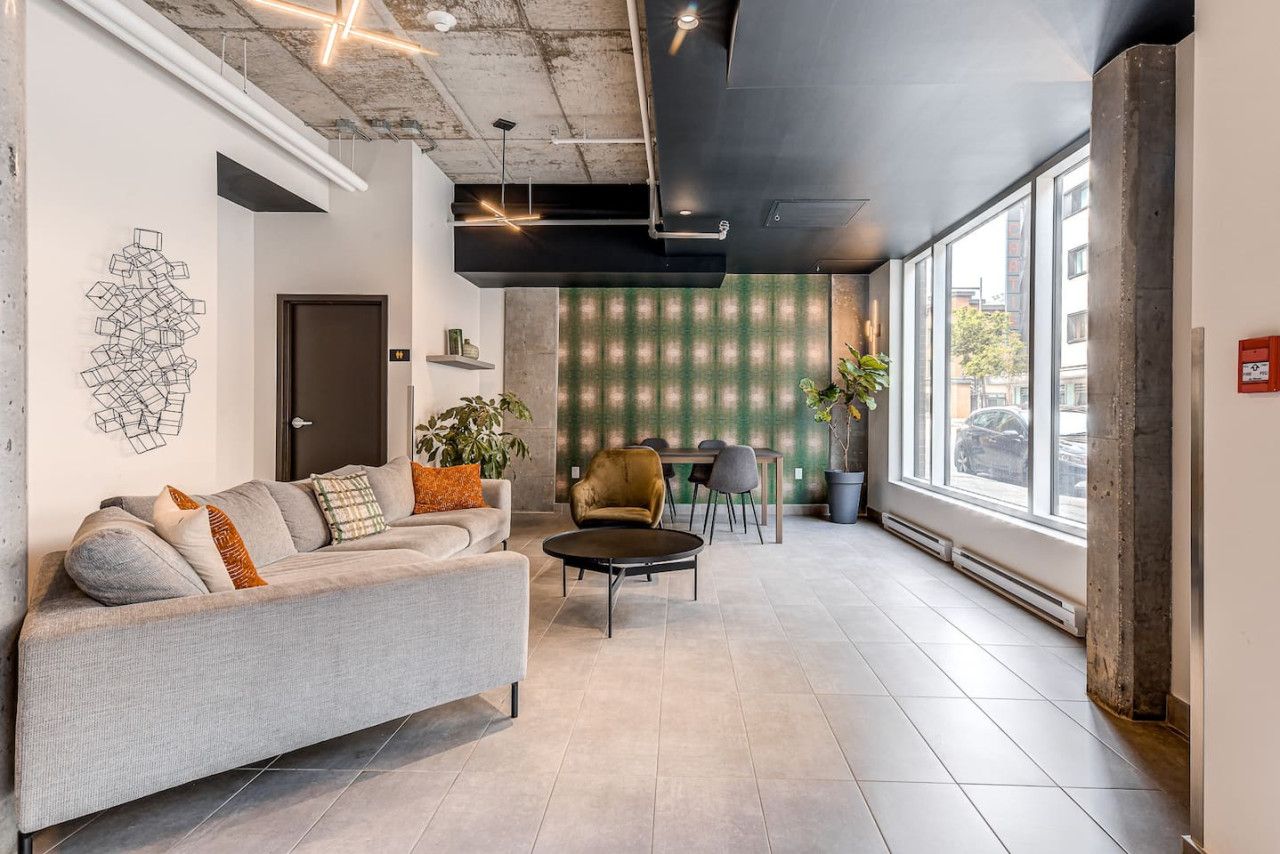 A modern interior with a grey sofa, a round coffee table, and a dining area with a green-striped wall and a plant.