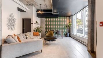 A modern interior with a grey sofa, a round coffee table, and a dining area with a green-striped wall and a plant.