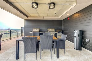 An outdoor patio with a table and chairs, a grill, and a trash can. - El Chico-Rooftop Pool (Québec)