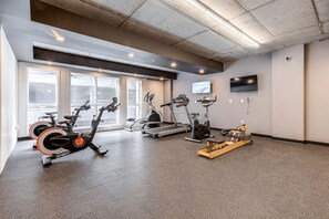 A gym with various cardio equipment, large windows, and a flat-screen TV on the wall. - El Chico-Rooftop Pool (Québec)
