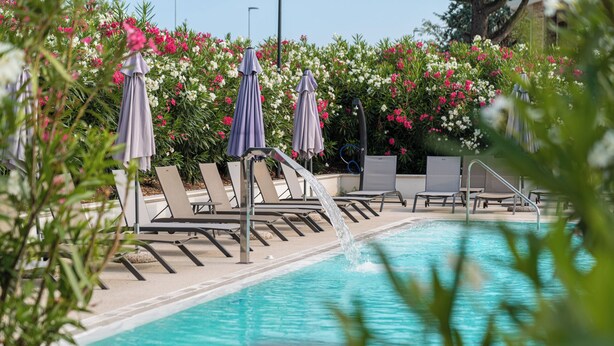 A pool area with lounge chairs and umbrellas, surrounded by flowering bushes. - I Campi Wine Relais (Lazise)