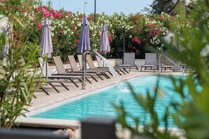 A pool area with lounge chairs and umbrellas, surrounded by flowering bushes.