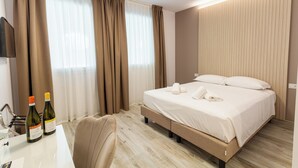 A hotel room with a bed, a desk with two bottles of wine, and a chair. - I Campi Wine Relais (Lazise)