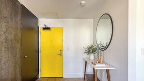 A hallway with a yellow door, a wooden floor, a white wall, and a mirror. - The Carter by AvantStay | 5th Floor, 15 Bedrooms (Nashville)