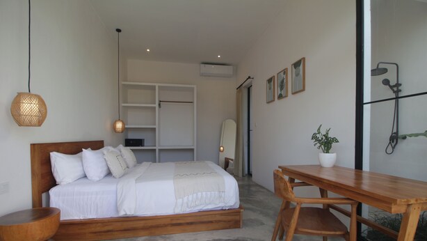 A bedroom with a wooden bed, a wooden desk, a potted plant, and a shower area. - Casa Batu Mejan (Canggu)