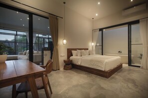 A bedroom with a large bed, a wooden table, a round side table, and a sliding glass door leading to a balcony. - Casa Batu Mejan (Canggu)