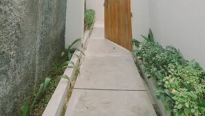 Un sendero estrecho que lleva a una puerta de madera, bordeado por paredes blancas y plantas verdes.