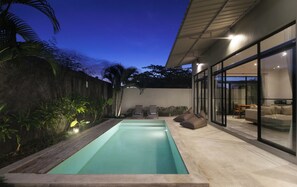 A modern outdoor pool area with a concrete deck, lounge chairs, and a glass-enclosed living space. - Casa Batu Mejan (Canggu)