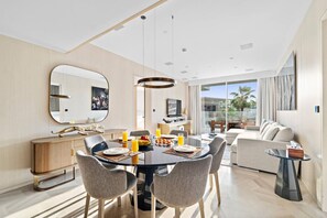 A modern hotel room with a dining area, a sofa, and a large window with a view.