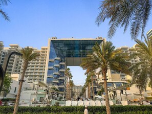 A modern building with a glass facade, surrounded by palm trees and other buildings.