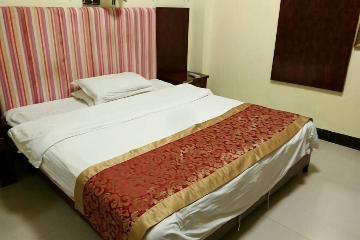 Una cama doble con colcha roja y blanca, cabecera a rayas y mesita de noche de madera con lámpara.