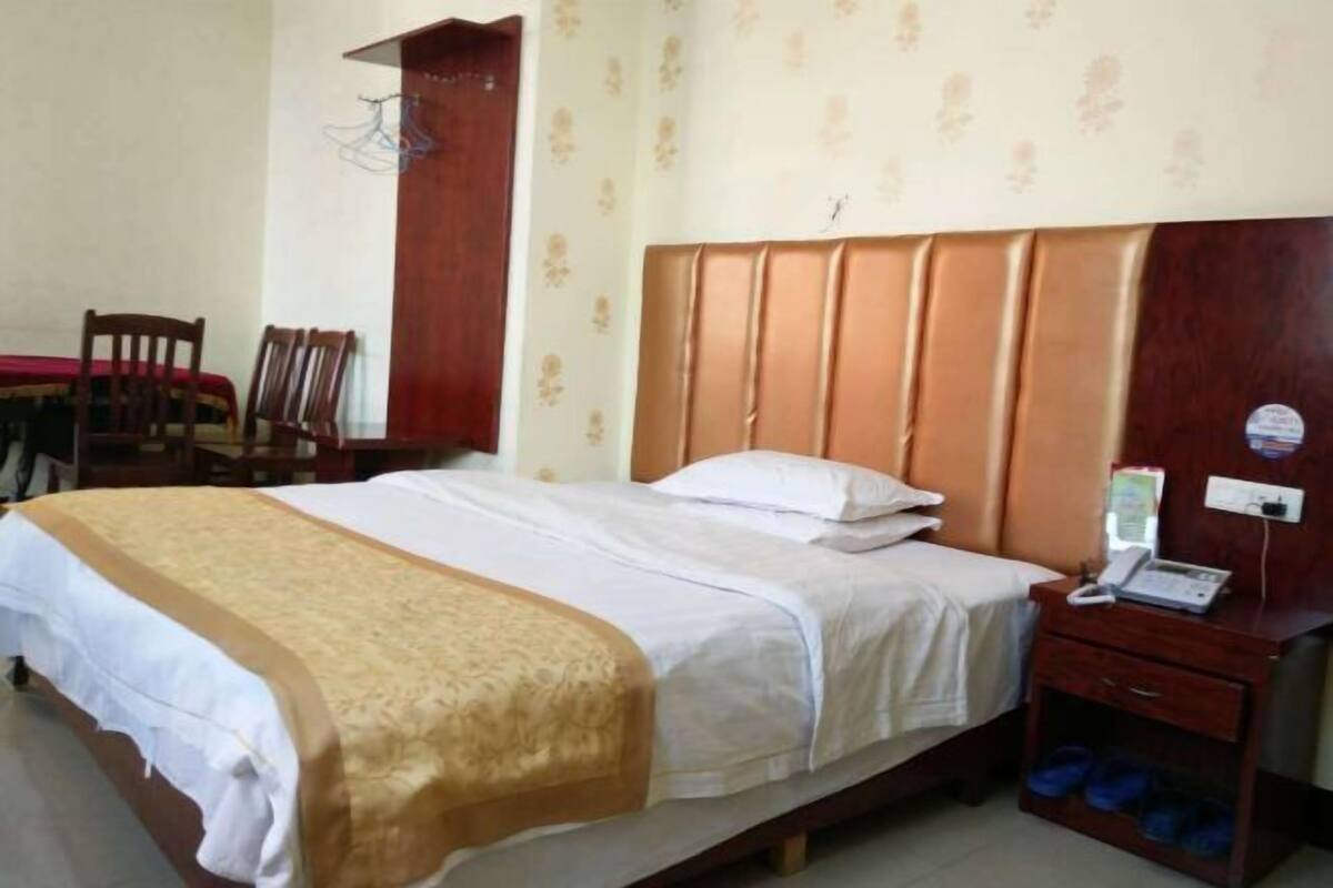 Habitación de hotel con una cama, una mesita de noche con teléfono, una silla y una pequeña mesa con mantel rojo.